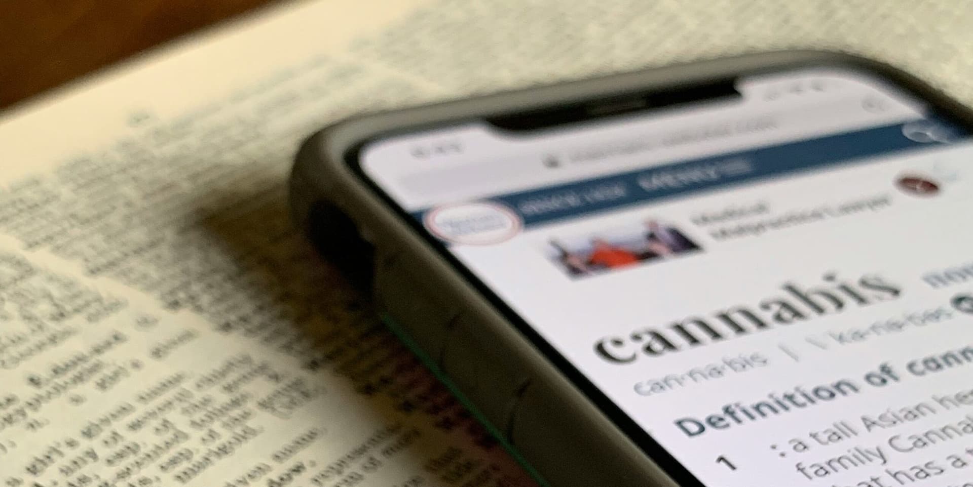 Smart Phone mit aufgeschlagener Dictionary-Seite mit dem Wort Cannabis liegt auf Printversion eines Wörterbuchs