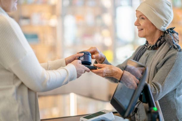 Krebskranke Frau nimmt eine Dose Cannabis von einer Apothekerin entgegen.